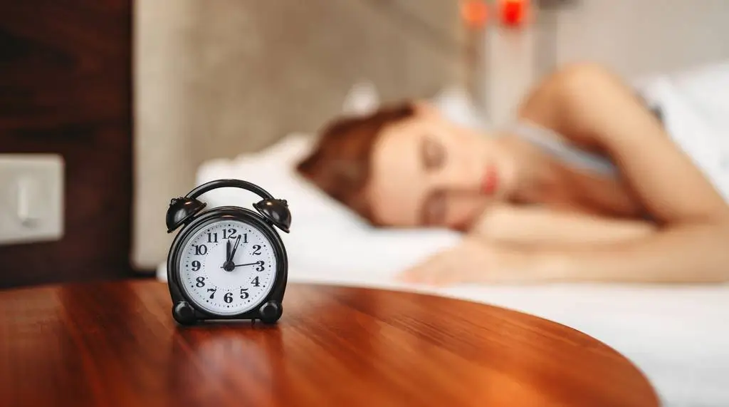 Une femme endormie paisiblement dans son lit avec un réveil au premier plan, illustrant l'accompagnement par l'hypnose pour retrouver le sommeil et vaincre l'insomnie au cabinet de Sandra Charpentier à Vesoul.